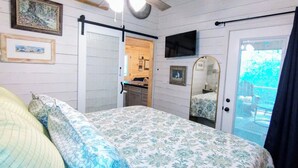 A bedroom with a bed, a ceiling fan, a door leading to a balcony, and framed pictures on the wall. - Charming NEW 2 BR Cottage, WiFi & Pet Friendly in Convenient Steele (Steele)