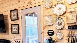 A kitchen with wooden walls, a black countertop, and a window. There are plates and utensils on the wall. - Charming NEW 2 BR Cottage, WiFi & Pet Friendly in Convenient Steele (Steele)