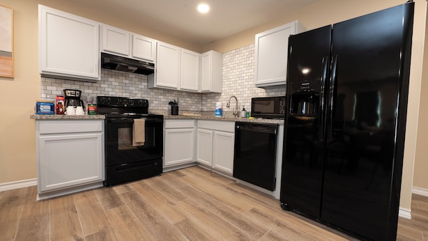 A modern kitchen with white cabinets, a black refrigerator, a microwave, and a stove. - Stunning Pet Friendly House with King Bed and Texas Size Backyard in Weslaco (Weslaco)