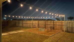 A backyard patio with string lights, a wooden fence, and outdoor furniture. - Stunning Pet Friendly House with King Bed and Texas Size Backyard in Weslaco (Weslaco)