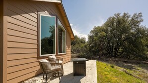 A wooden house with a patio, a wicker chair, and a trash bin. - New 1 Bed Near Yosemite, Fire Pit, Washer, Dryer (Mariposa)