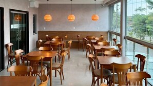 A modern dining area with wooden tables and chairs, pendant lighting, and large windows offering a view of greenery. - Gran Amazon Av. Brasill (Belem)