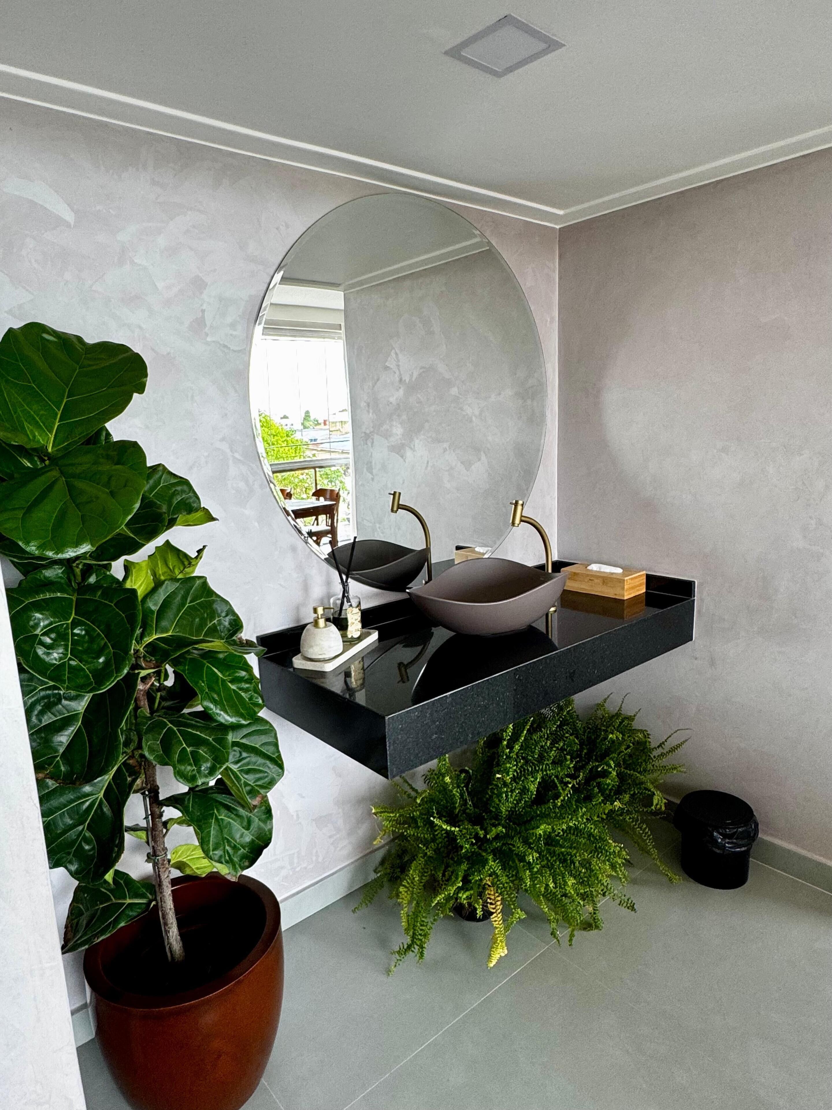 Un baño moderno con tocador negro, un espejo redondo y una planta en maceta.