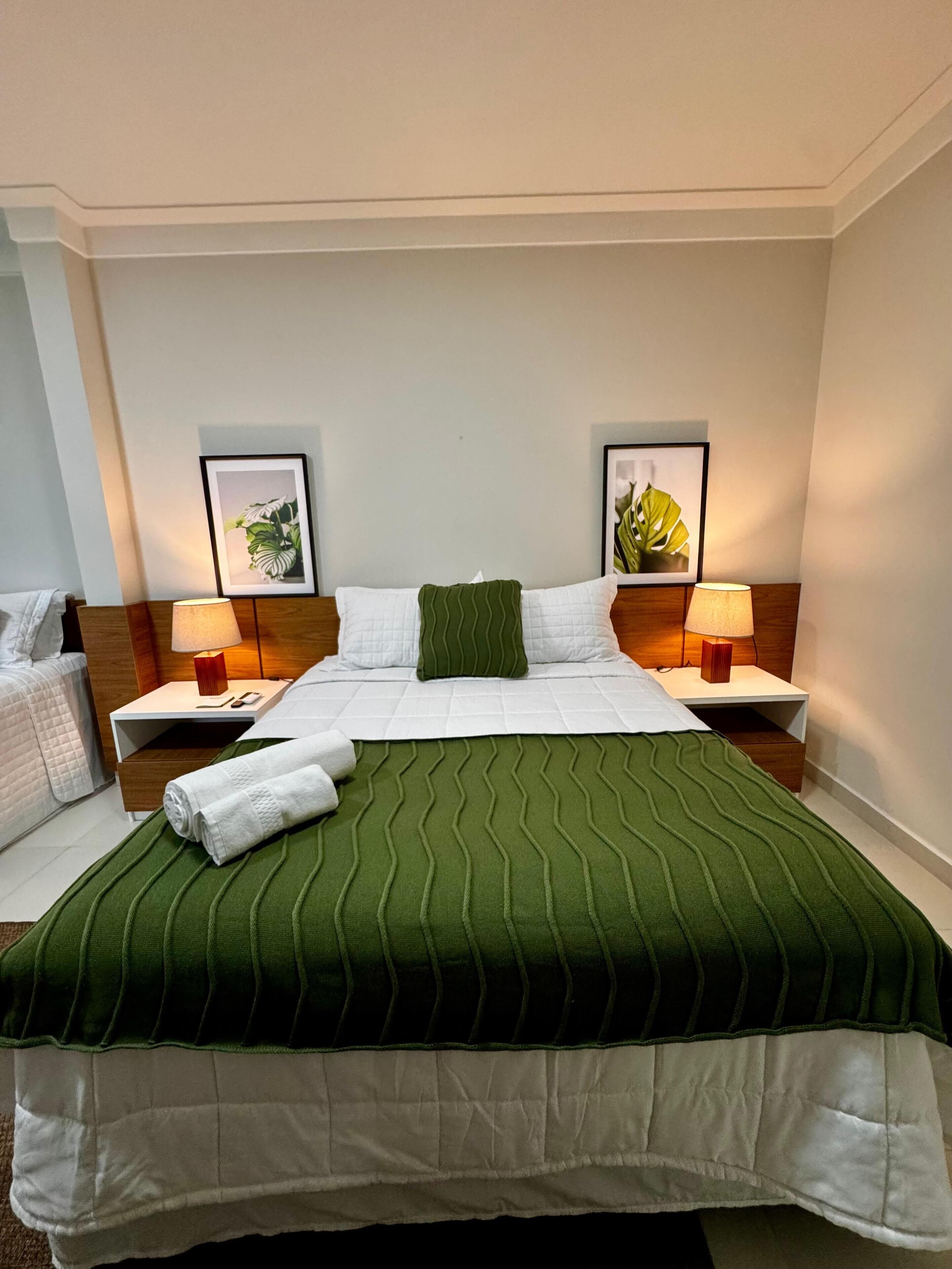 Une chambre d’hôtel avec un lit soigneusement fait, deux lampes de chevet et deux tableaux encadrés accrochés au mur.