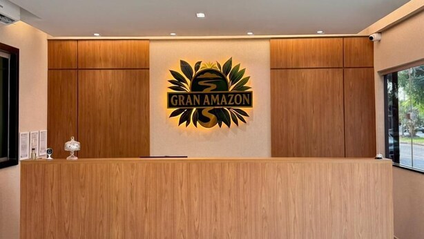 A reception desk with a logo, wooden paneling, and a view of the outdoors. - Gran Amazon Av. Brasill (Belem)