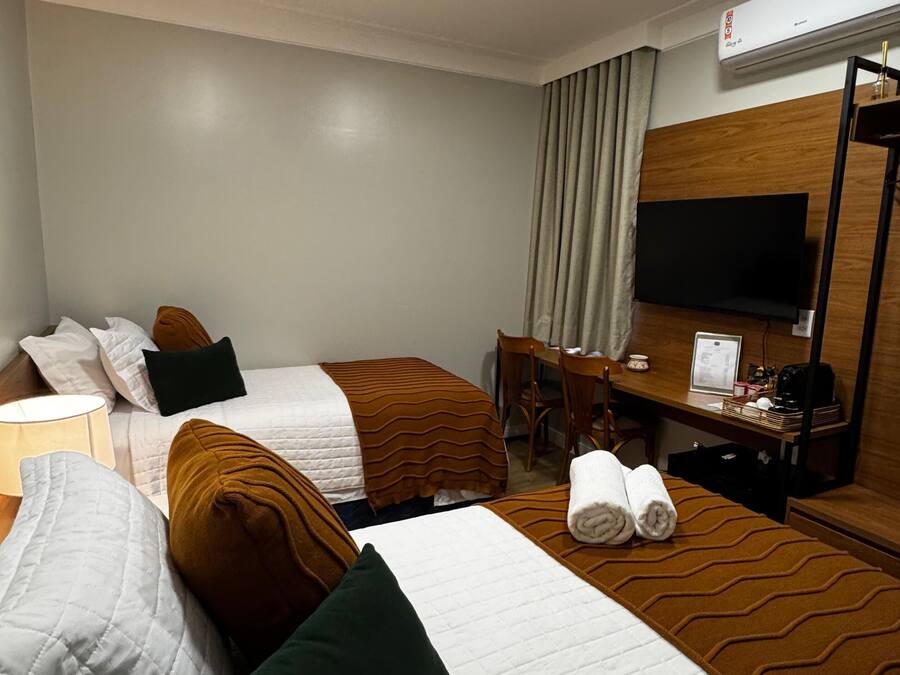 A hotel room with two beds, a desk, a chair, a television, and an air conditioning unit.