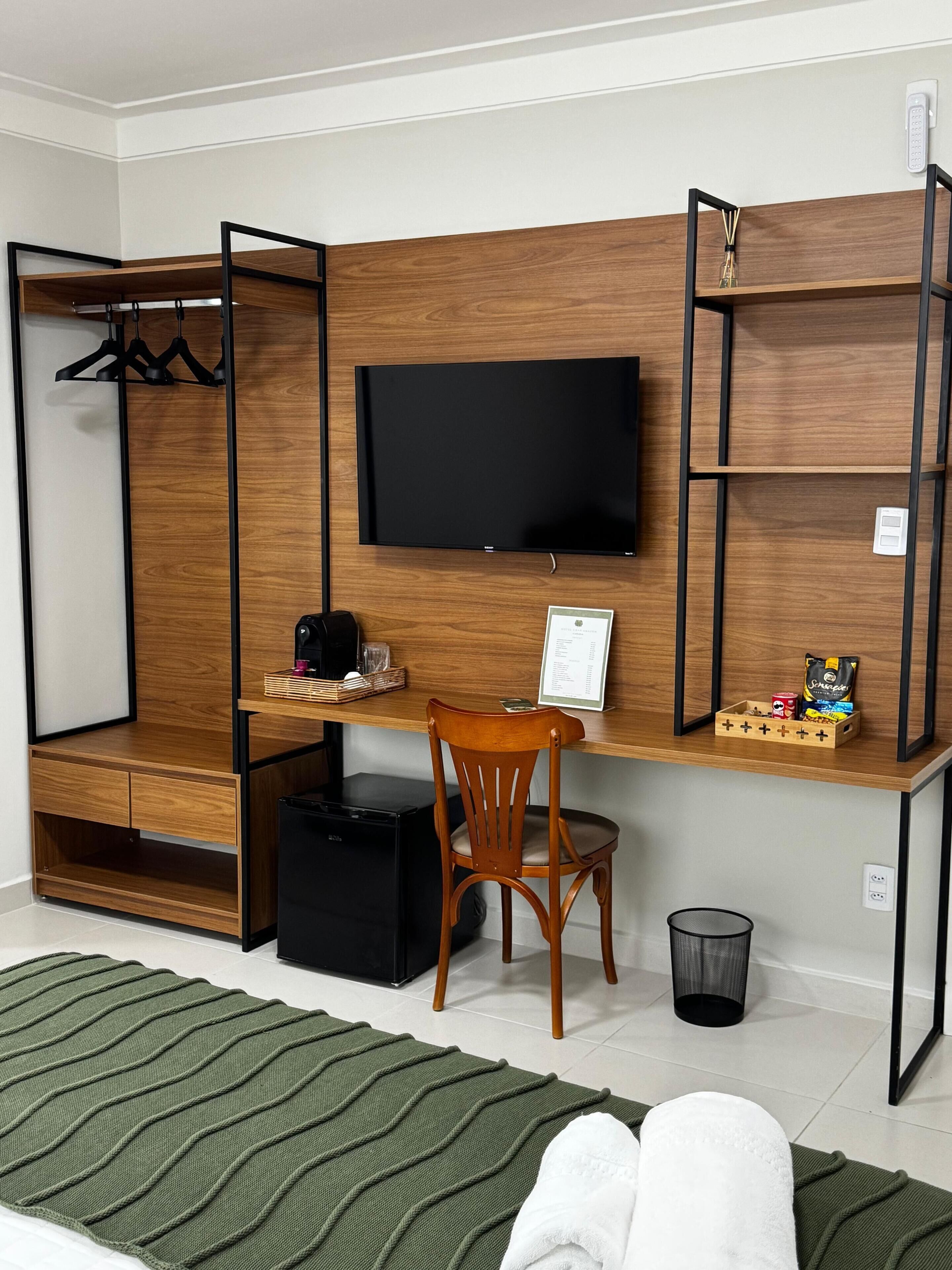 A compact room with a wooden desk, a television, a chair, a small black trash bin, and a green area rug.