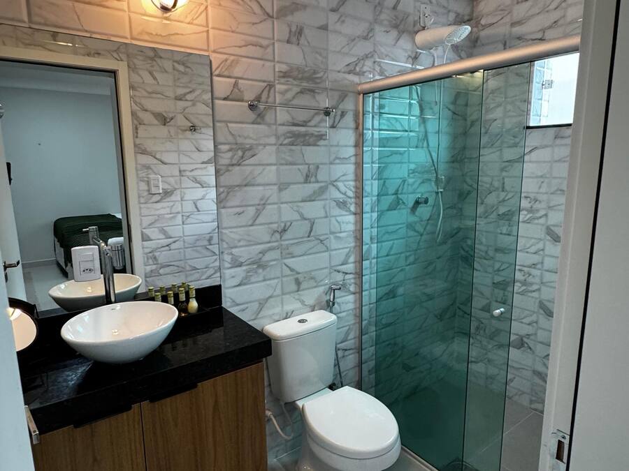 A modern bathroom with marble-patterned walls, a black countertop, wooden cabinets, a white sink, a toilet, and a glass-enclosed shower.