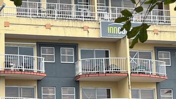 A multi-story building with balconies, a visible storefront with a sign, and a tree in the foreground.