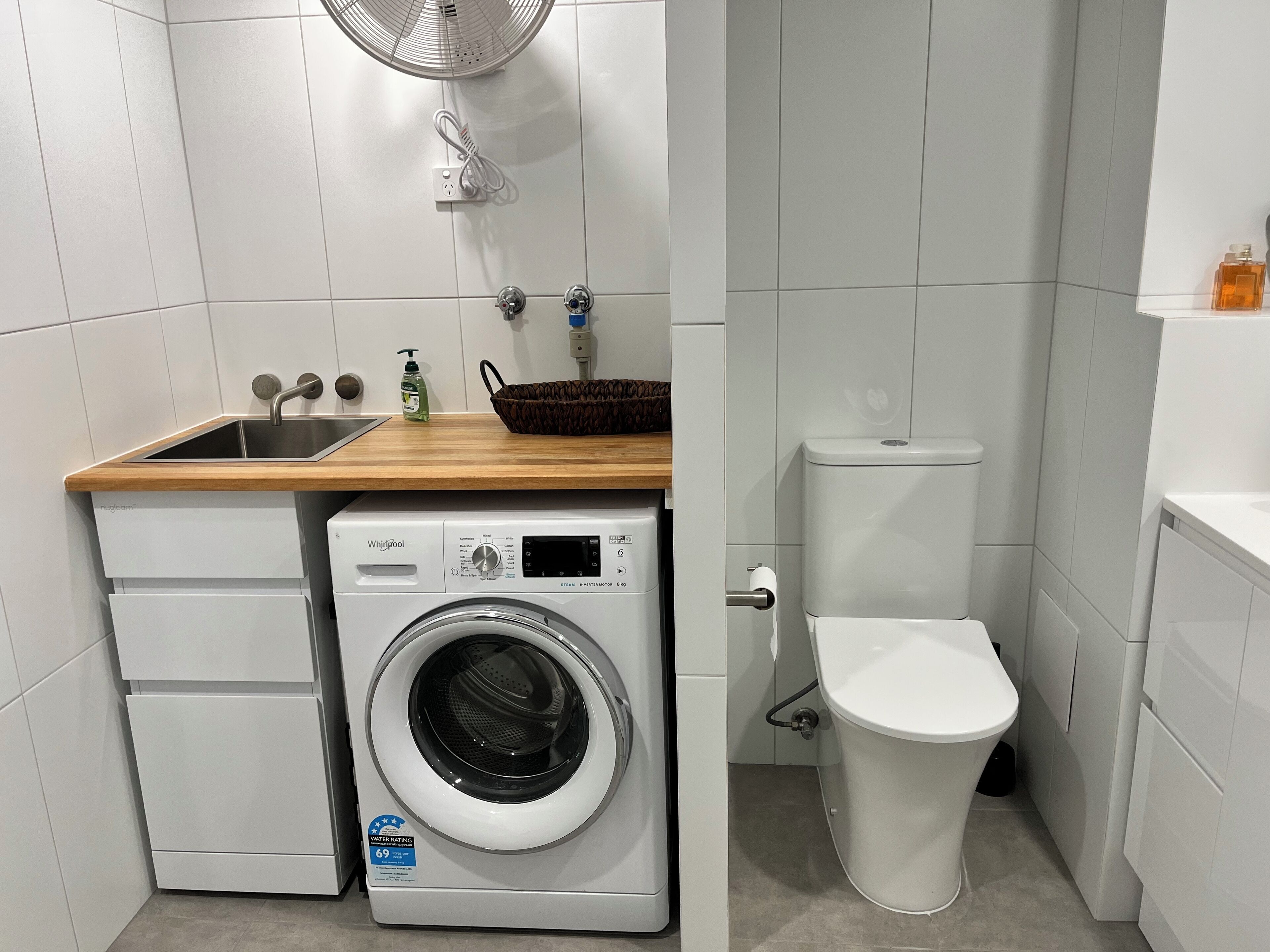A compact laundry room with a front-loading washer, a sink, and a toilet.