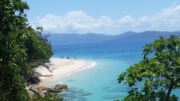 Una playa con agua turquesa cristalina, rodeada de terreno rocoso y vegetación densa.