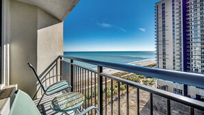 A balcony with a view of the beach and ocean, a high-rise building, and a table with chairs. - Ocean View Efficiency, Newly Renovated,Jacuzzi Tub (Myrtle Beach)