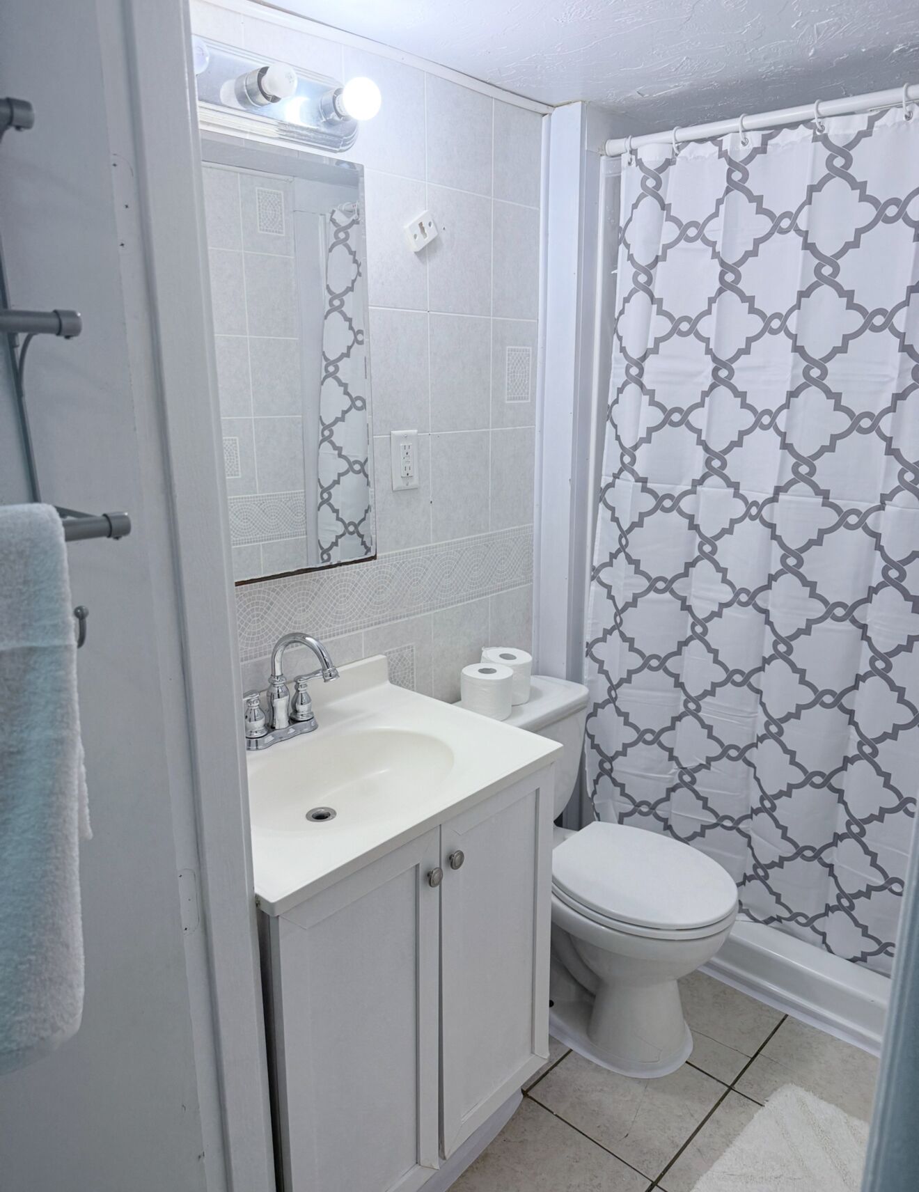 Ein Badezimmer mit einem weißen Waschbecken, einer Toilette und einem Duschvorhang mit geometrischem Muster.