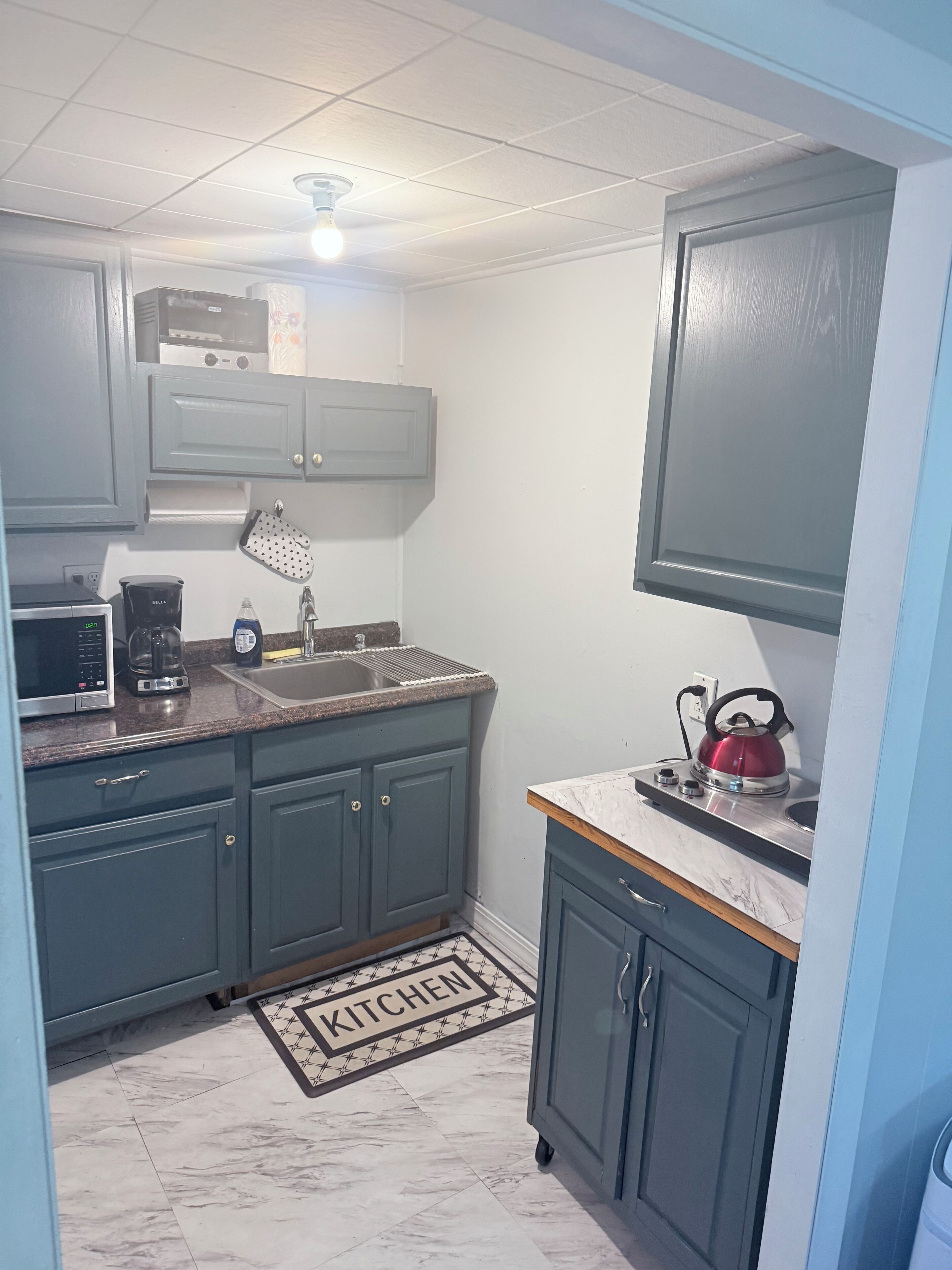 Una cocina compacta con armarios azul oscuro, un microondas, una cafetera, un hervidor y un lavamanos.