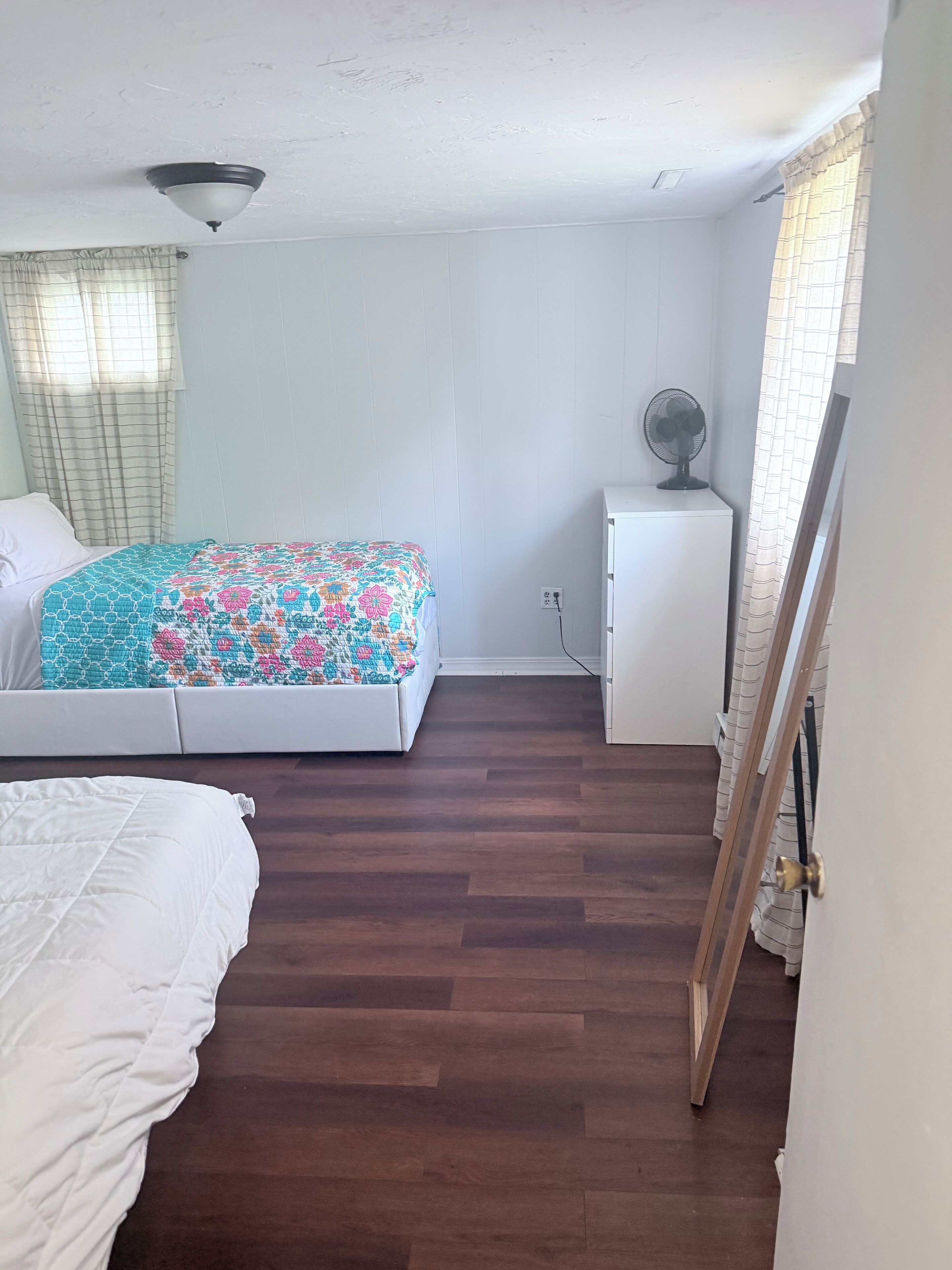 Een slaapkamer met een bed, nachtkastje, ventilator en kledingkast.