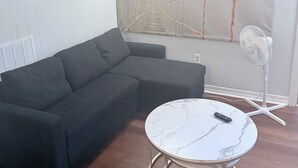Una sala moderna con un sofá modular, una mesa redonda de mármol, un ventilador de pared y un mural de un puente colgante.