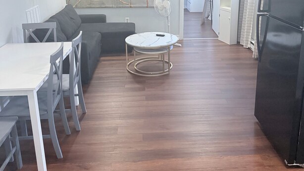 Un amplio salón con suelo de madera, un sofá, una mesa de comedor con sillas, una mesita redonda y un refrigerador negro.