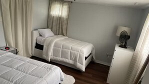 Un dormitorio con dos camas, una mesita de noche, una lámpara y un armario pequeño.