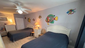 A room with two beds, a ceiling fan, a dresser, a nightstand, and wall art. - Beachfront Condo (Summer Sands #214) with outdoor pool & BBQ grills! (North Wildwood)