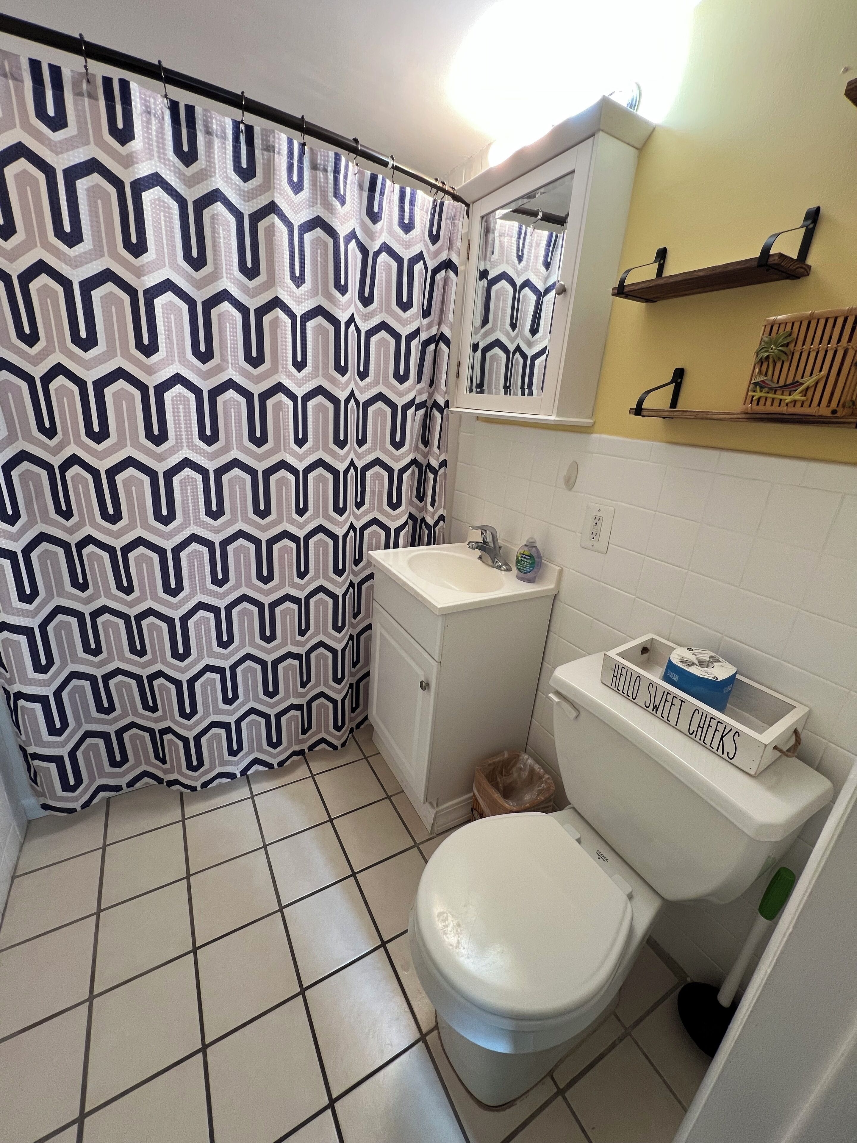 Een badkamer met een wit toilet, een wastafel, een spiegel en een douchegordijn met een geometrisch patroon.