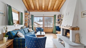 A cozy living room with a wooden ceiling, a fireplace, a sofa, a chair, and a bookshelf. - Luxury chalet St. Moritz with panoramic mountain view (Madulain)