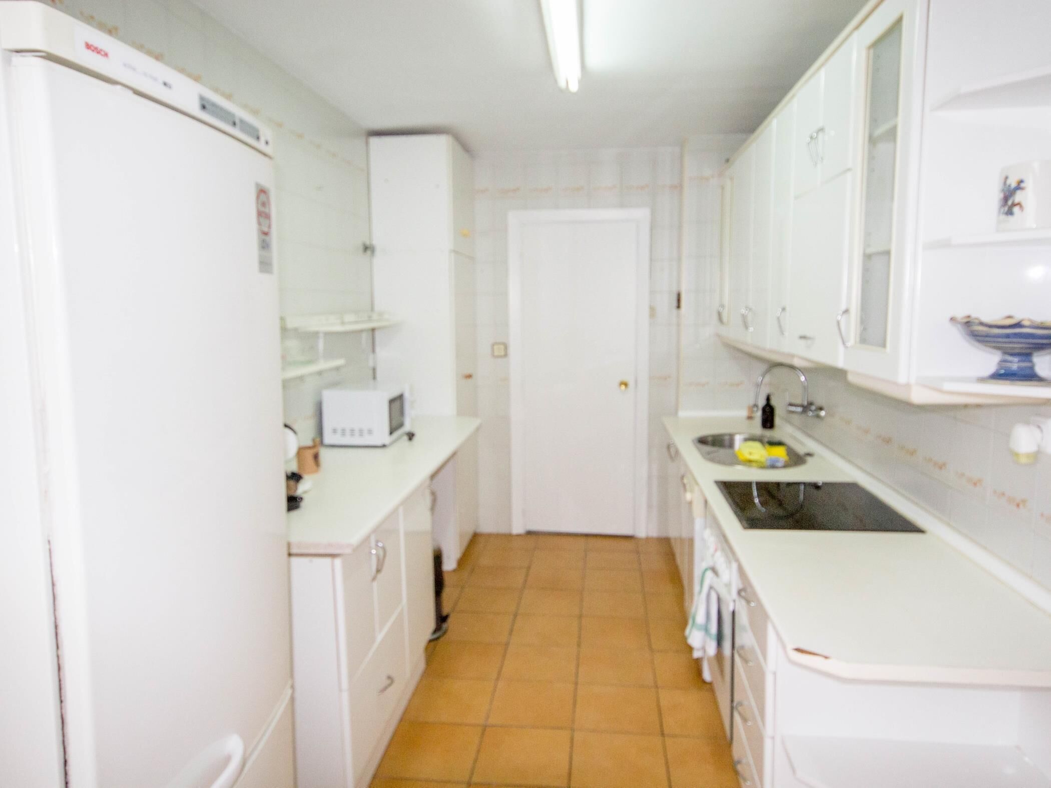 Una cocina estrecha con armarios blancos, un lavamanos y un refrigerador.