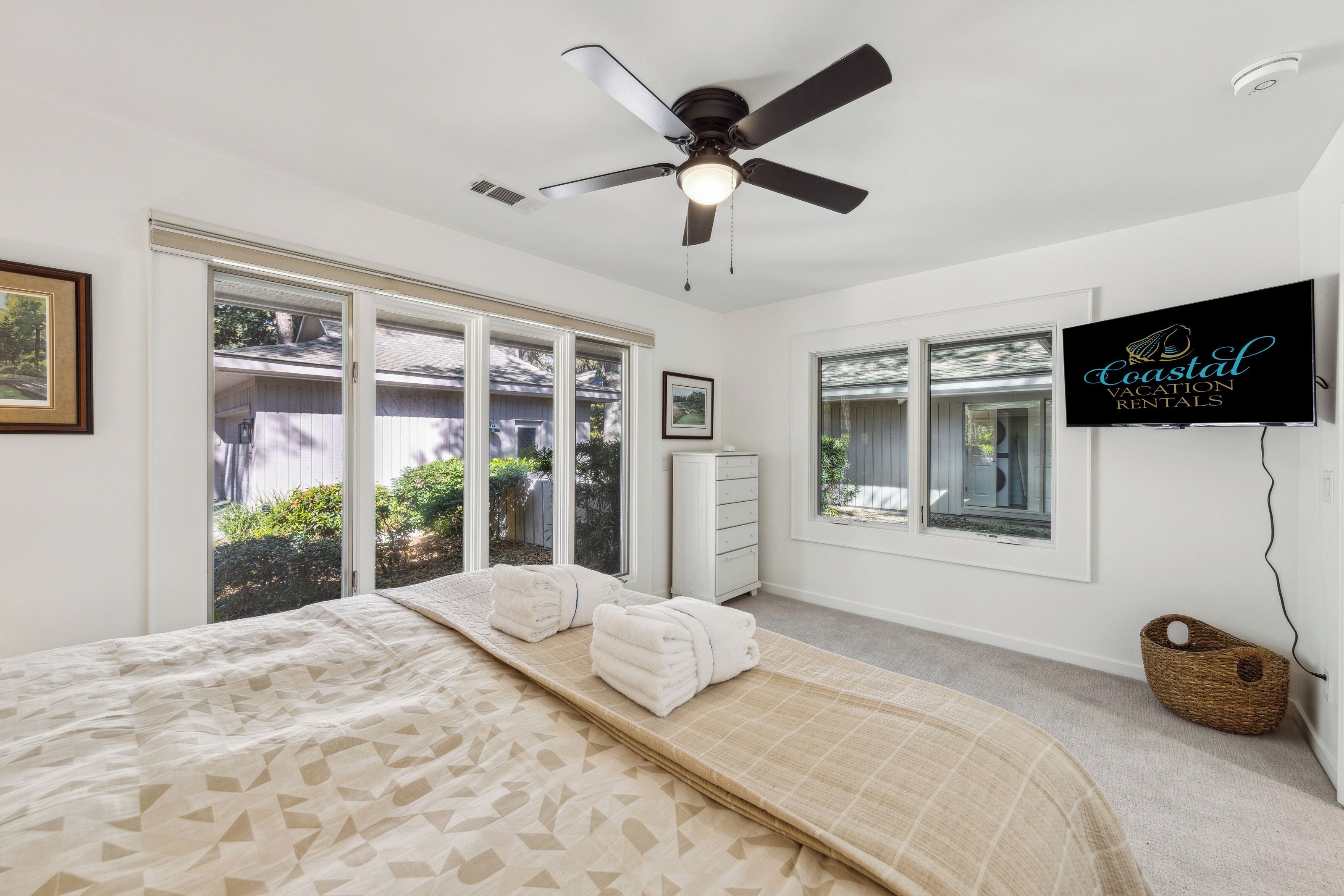 Un dormitorio con cama, ventilador de techo, televisión y puerta corrediza de vidrio al exterior.