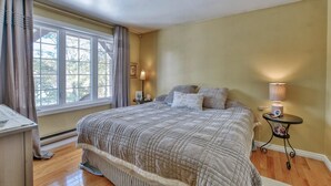 A bedroom with a large bed, a nightstand, a lamp, and a window with curtains. - cozy family house for rent on the ski mountain (Saint-Sauveur)