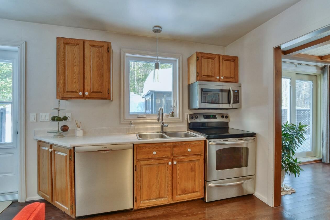 A kitchen with wooden cabinets, a stainless steel oven, and a microwave. - cozy family house for rent on the ski mountain (Saint-Sauveur)