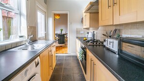 A modern kitchen with wooden cabinets, a black countertop, a built-in oven, and a window providing natural light. - Golden Triangle 2 bed + Garden + Parking (Norwich)