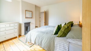 A bedroom with a bed, a dresser, a fireplace, and a door. - Golden Triangle 2 bed + Garden + Parking (Norwich)