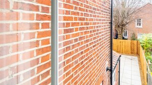 A brick exterior wall with a metal gutter and a wooden fence. - Golden Triangle 2 bed + Garden + Parking (Norwich)