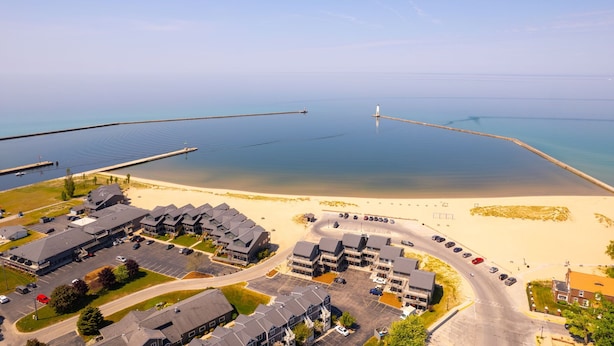 An aerial view of a coastal area with a beach, a pier, and a row of multi-story buildings with parking lots.