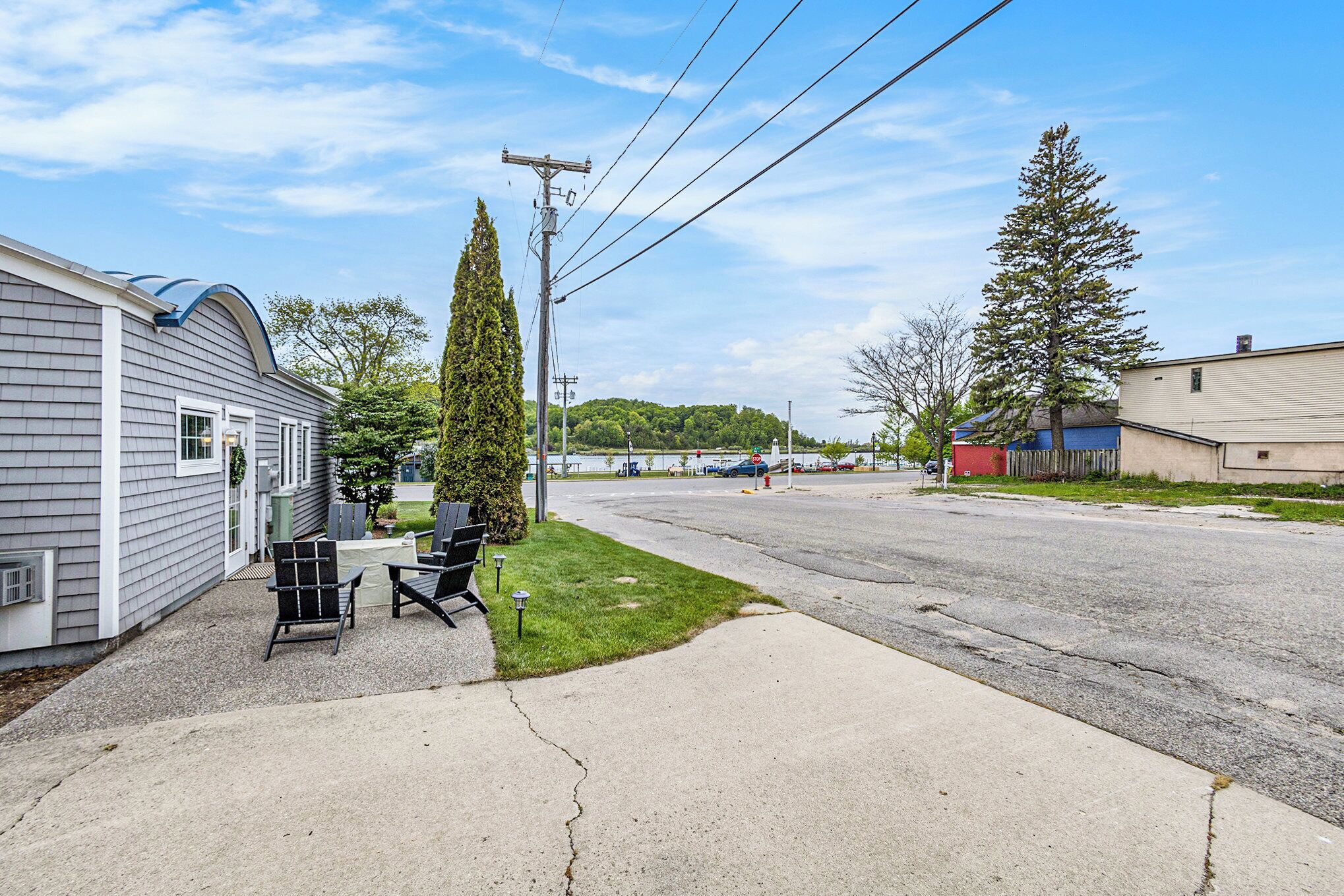 A residential street with houses, a driveway, and a grassy area with outdoor furniture.