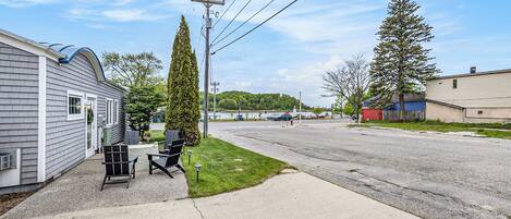 A residential street with houses, a driveway, and a grassy area with outdoor furniture.