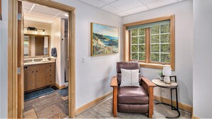 A bathroom with a wooden vanity, a mirror, and a painting of a coastal scene.