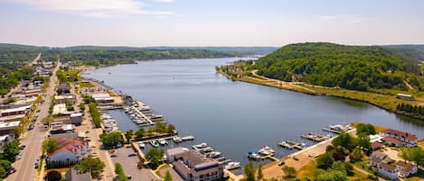 Vista aérea de un pueblo junto al lago, con un puerto deportivo, edificios residenciales y una carretera que bordea el agua.