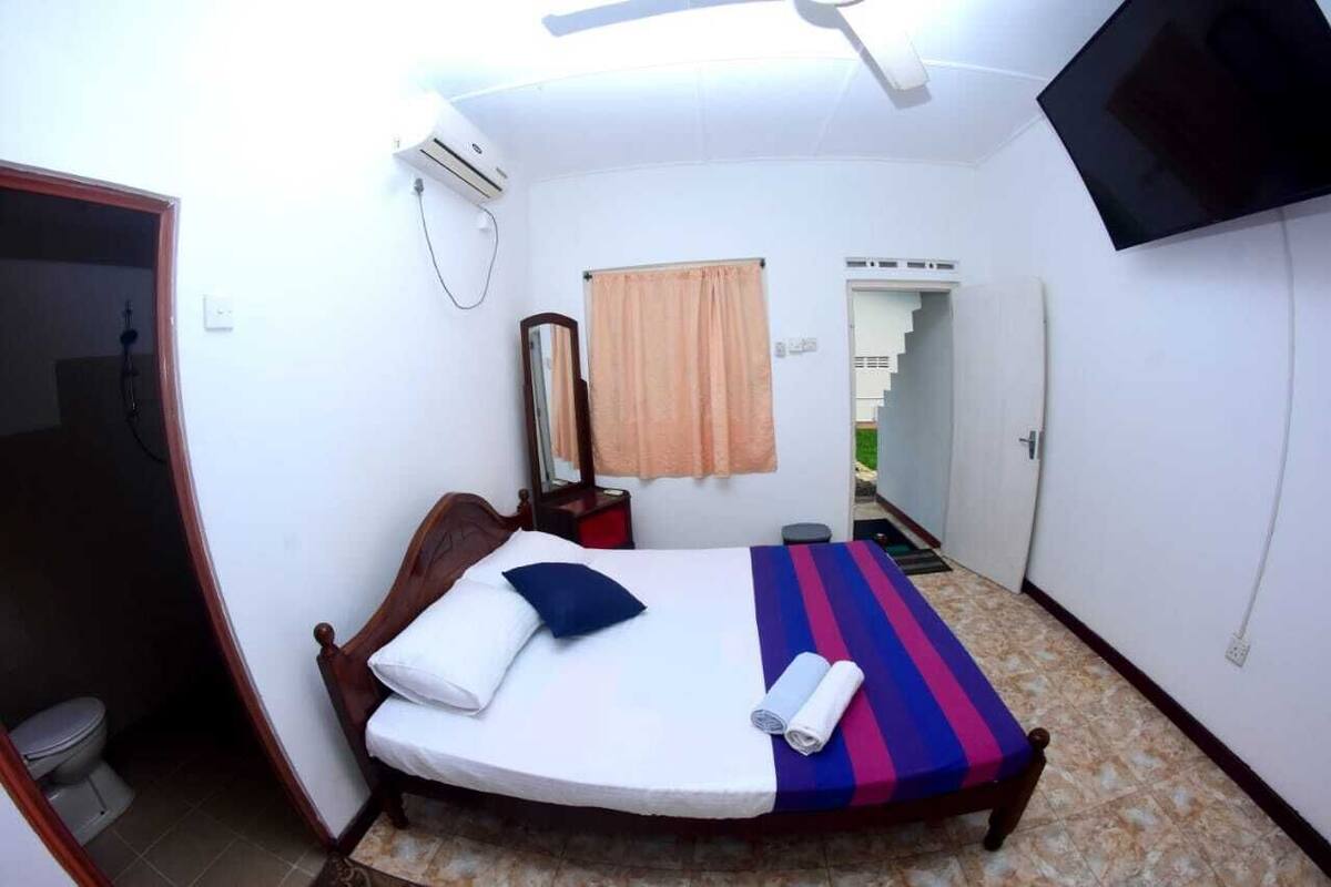 Una camera da letto con un letto, una TV, uno specchio e una finestra con tende.