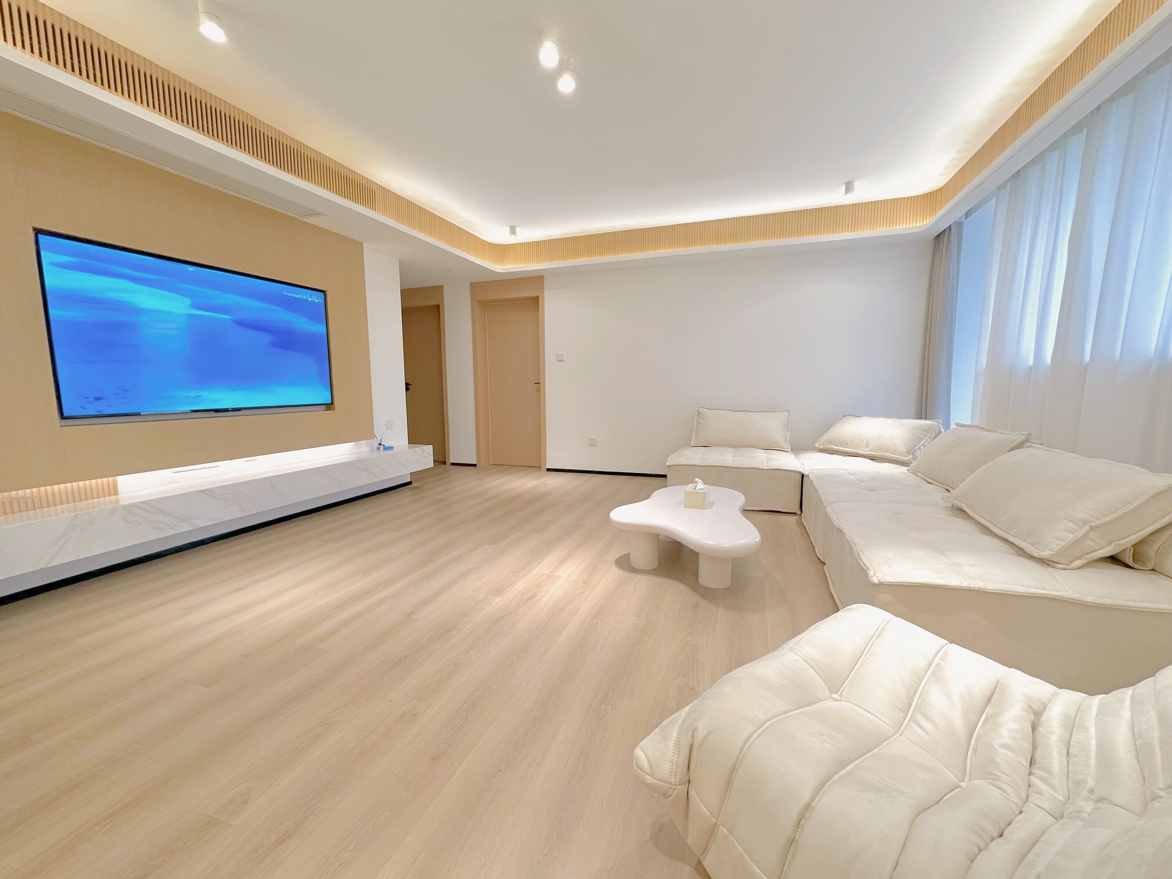 A modern living room with a large flat-screen TV, a sofa, and a coffee table.