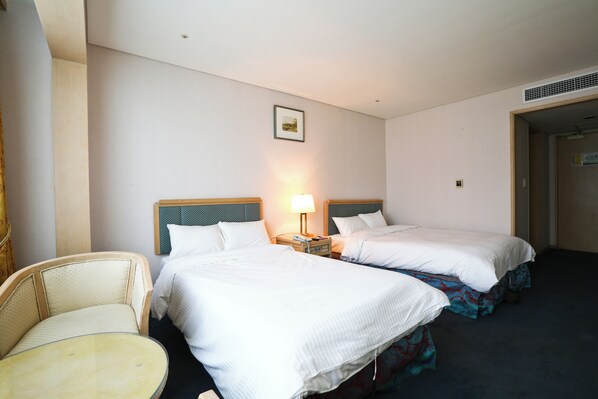 A hotel room with two beds, a chair, and a nightstand with a lamp.