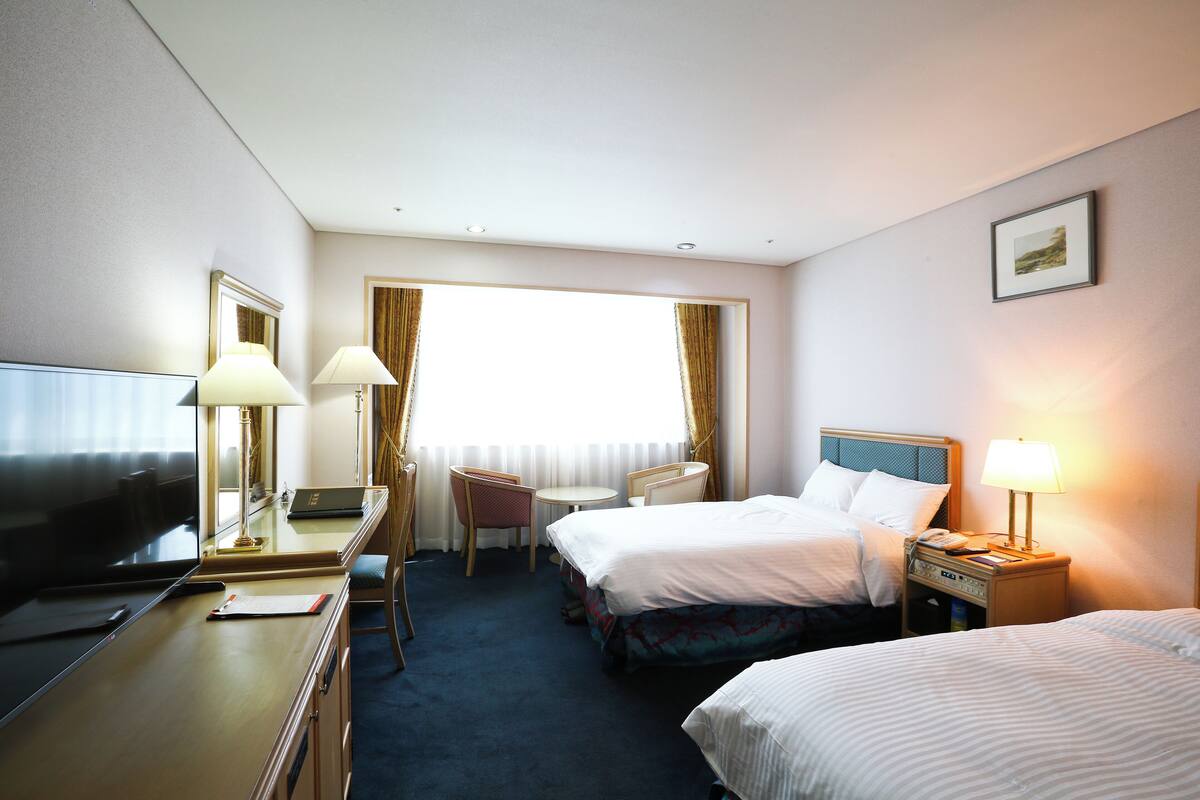 A hotel room with two beds, a desk with a computer, a TV, and a chair.