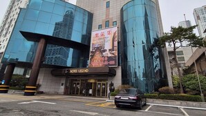 A modern hotel with a glass facade, a prominent sign for the hotel, and a parking area in front. - Legend Hotel (Daejeon)