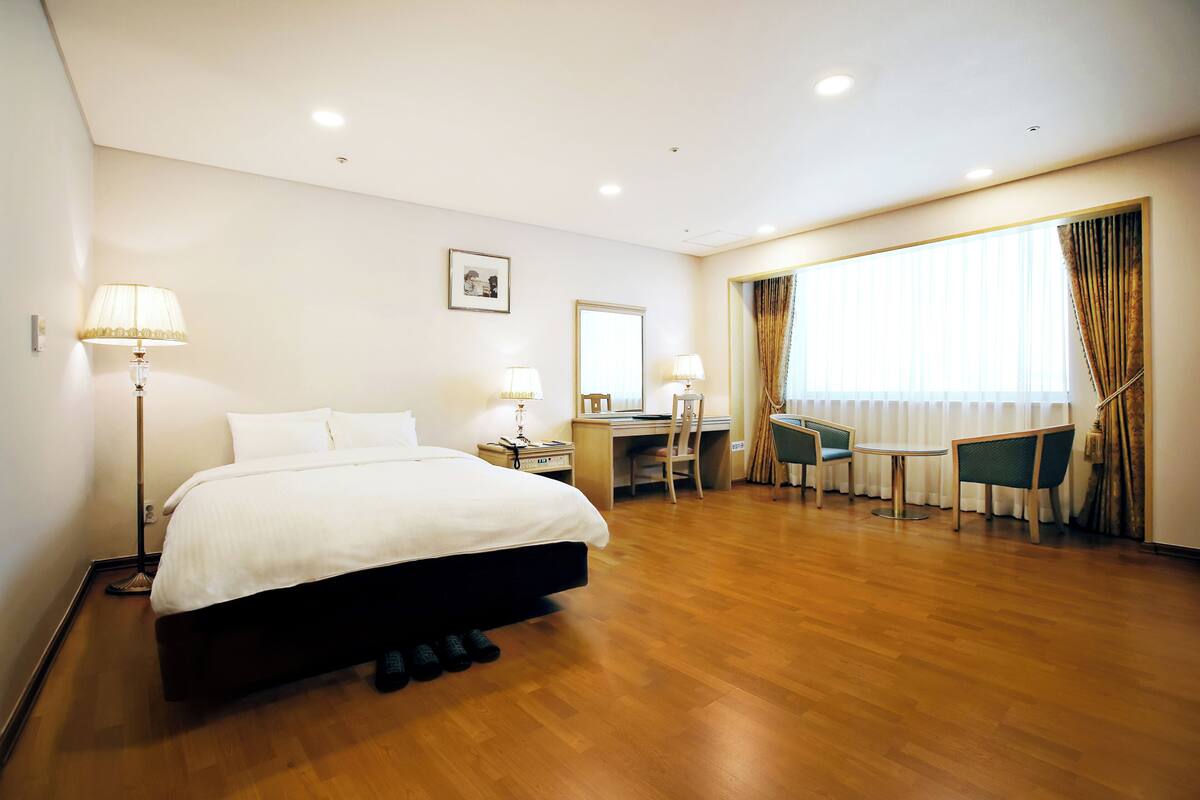 A hotel room with a large bed, a desk, a chair, and a small table.