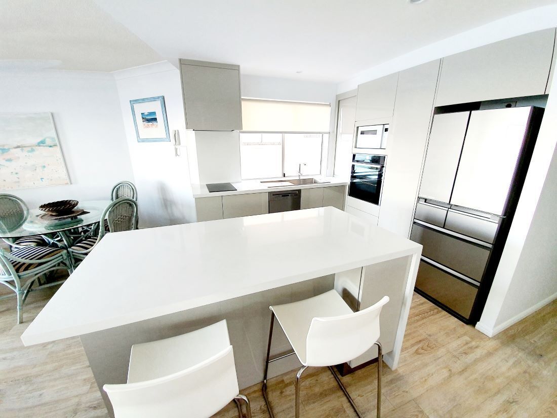 A modern kitchen with a central island, white bar stools, and a dining area with a table and chairs.