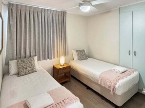 Une chambre avec deux lits simples, une table de chevet avec une lampe, une armoire et un ventilateur de plafond.