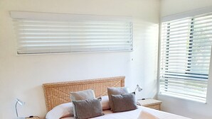 Une chambre à coucher avec un grand lit, deux tables de chevet, une commode et une fenêtre avec des stores.