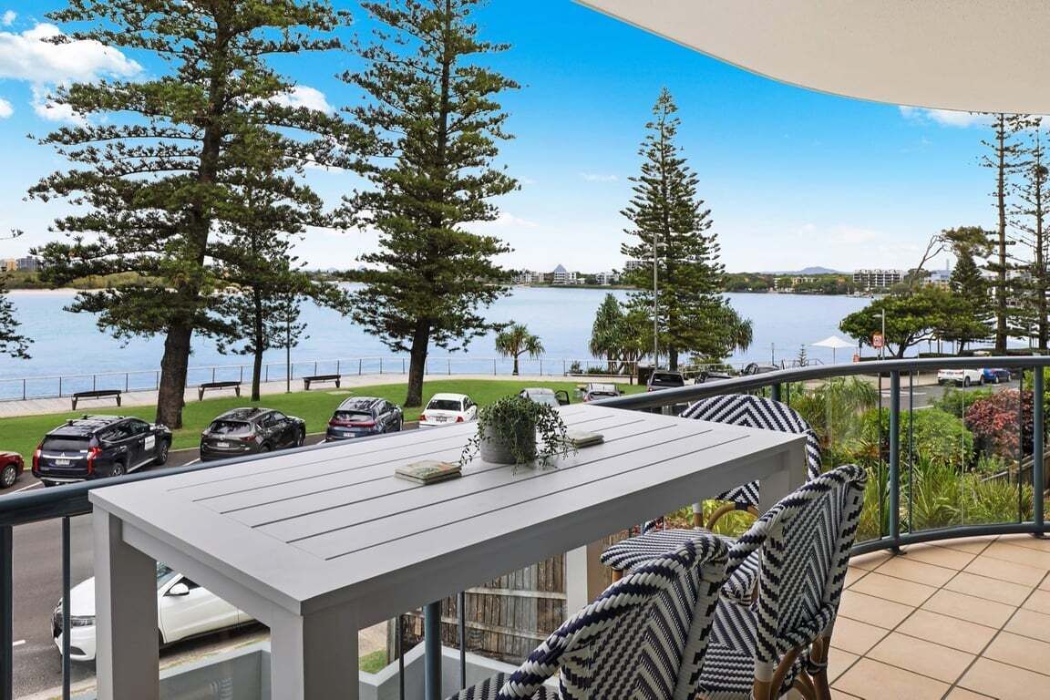 A balcony with a view of a lake, surrounded by trees and parked cars.