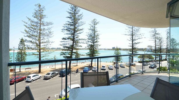 A balcony with a view of a parking lot, beach, and ocean.
