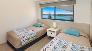 Un dormitorio con dos camas, una mesita de noche y una ventana con vistas a un cuerpo de agua y un árbol.