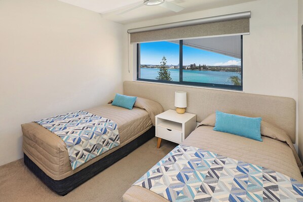 A bedroom with two beds, a nightstand, and a window with a view of a body of water and a tree.